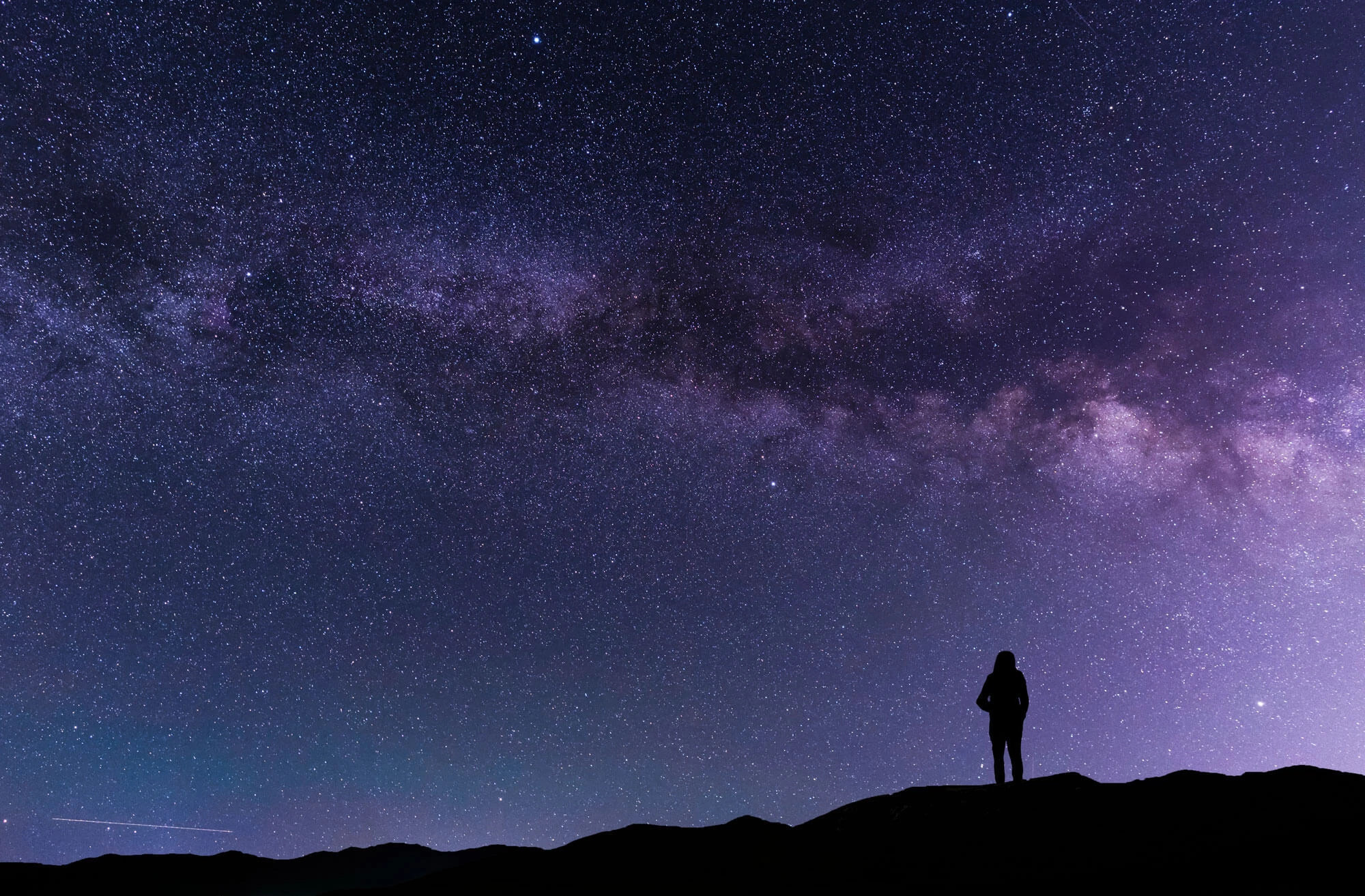 A silhouette stands on in the hill and looks at the Milky Way galaxy 1